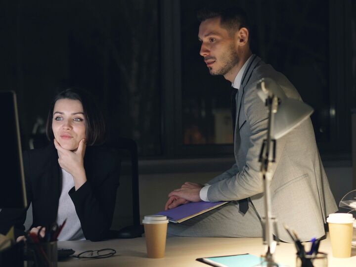 Two coworkers at a desk in the evening, looking at a computer screen together